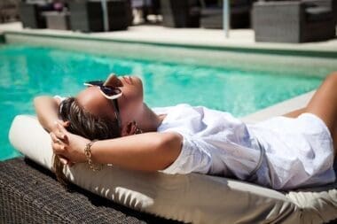 Beautiful young woman resting on a chaise longue next to a swimming pool