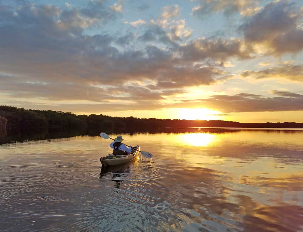 A man paddles his kayak through the Everglades at sunset