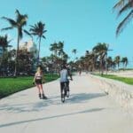 Rear view of a woman inline skating on the Miami Beach Boardwalk near Lummus Park, alongside a man on a bicycle.