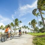 Individuals of all ages cycling through Lummus Park along the Miami Beach Boardwalk.