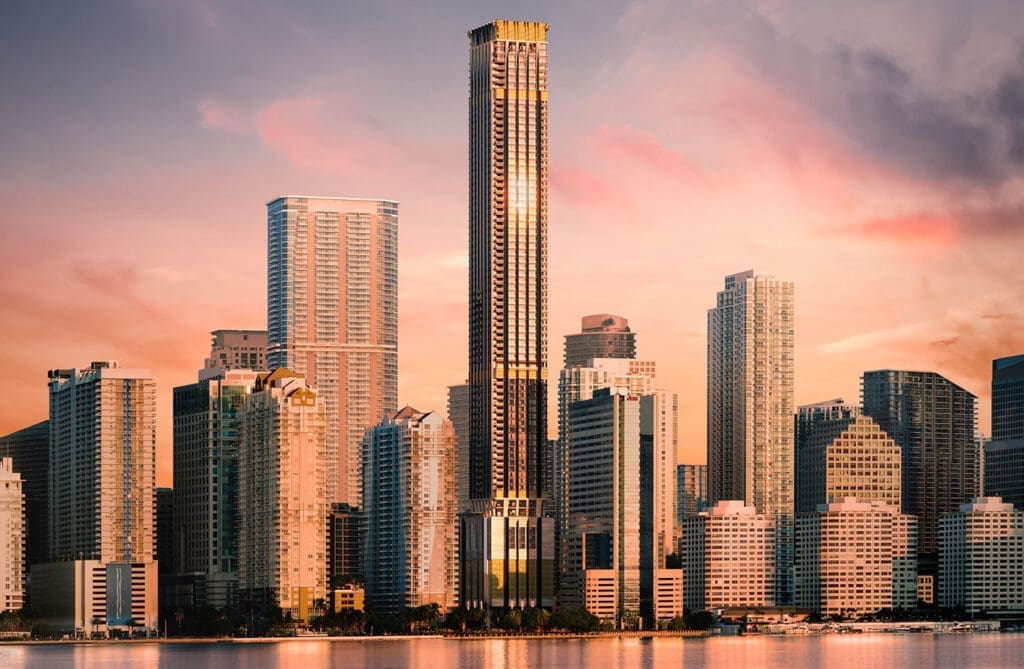 The Miami skyline at sunset, with a prominent new, tall skyscraper at the center, reflecting the golden light. Other buildings and a body of water are in the foreground, under a pink and orange cloudy sky.