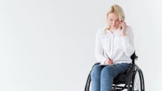 A woman with multiple sclerosis is seen from the front, sitting in a wheelchair as she works and talks on the phone