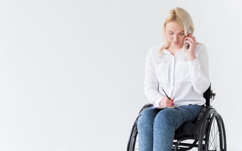 A woman with multiple sclerosis is seen from the front, sitting in a wheelchair as she works and talks on the phone