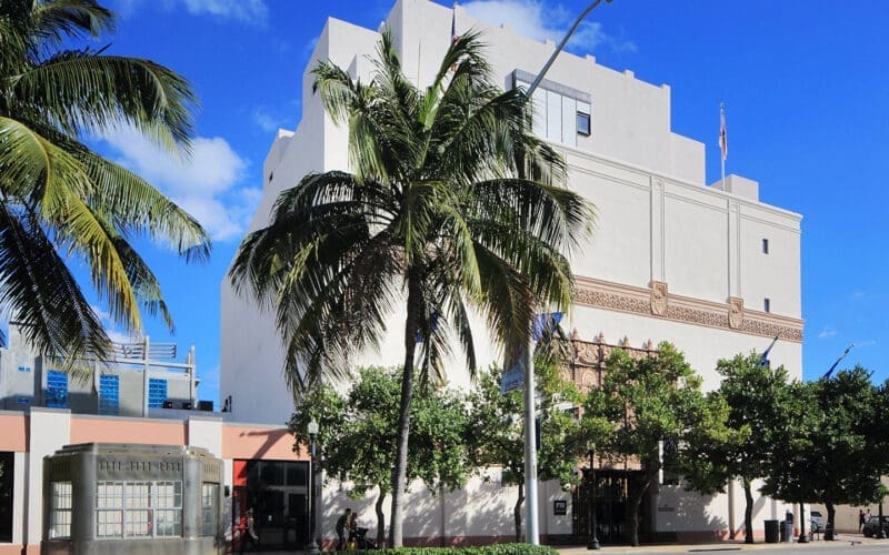 The exterior of The Wolfsonian-FIU museum, a white building with palm trees in the foreground, under a blue sky.