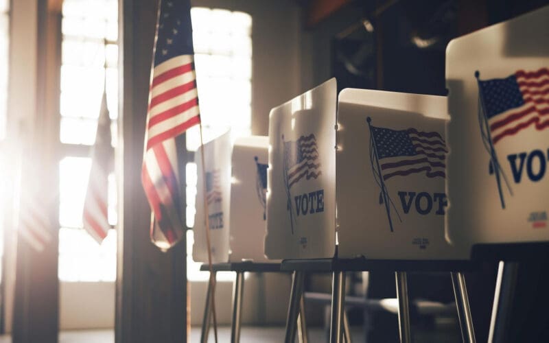 Voting stations neatly arranged against a wall decorated with US flags