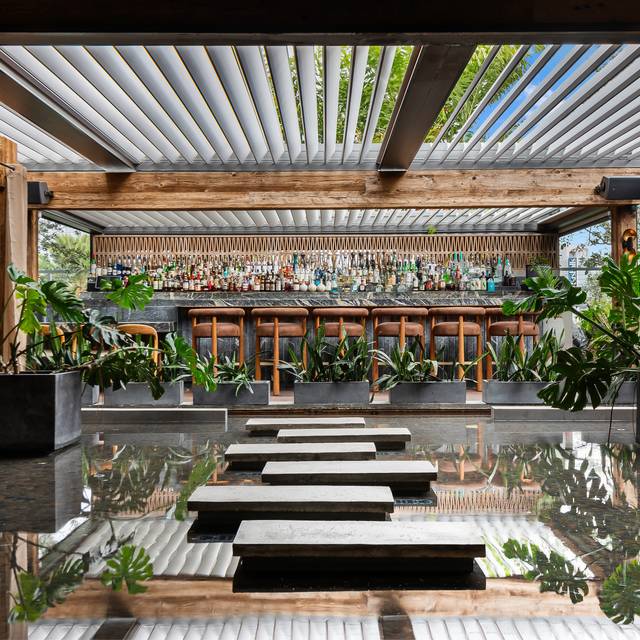 A panoramic view of MILA Miami's vibrant rooftop dining and lounge, showing elegantly set tables, ambient lighting, and the illuminated Miami Beach skyline at dusk or night.