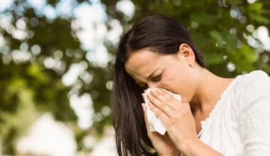 A brunette woman is blowing her nose due to her allergies