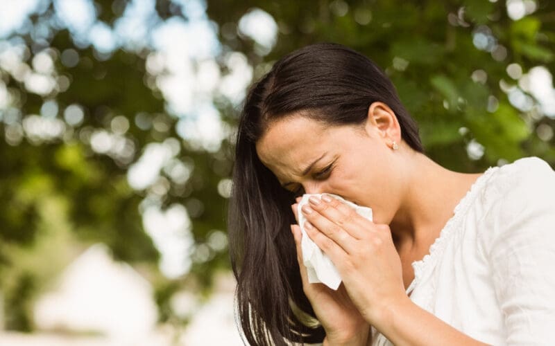 A brunette woman is blowing her nose due to her allergies