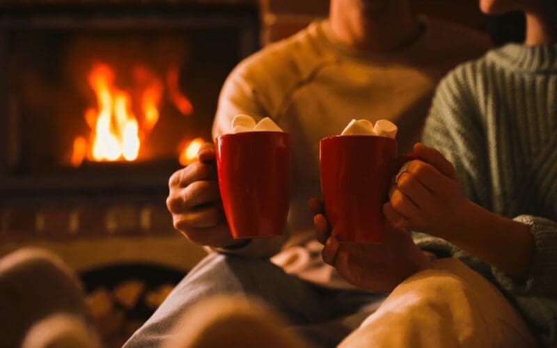 A charming couple enjoying sweet cocoa by the fireplace indoors, captured in a close-up shot