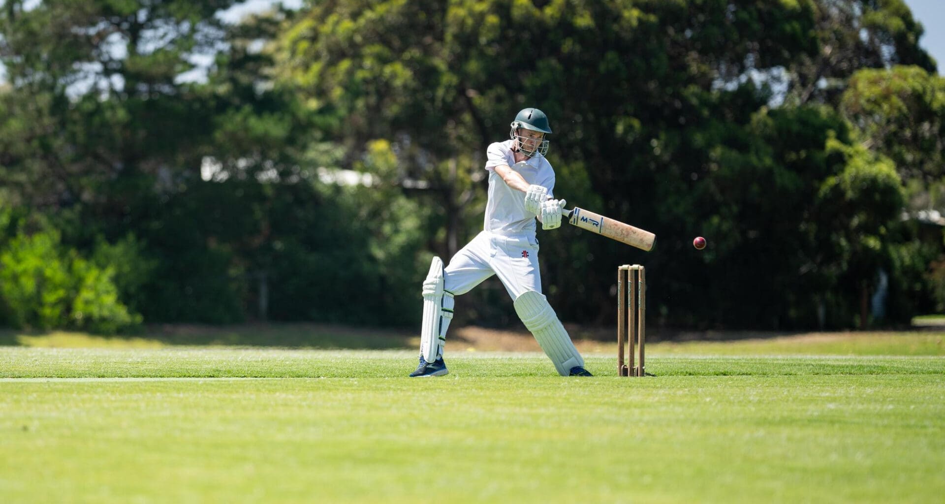 A cricketer is batting on a green cricket oval during a local match in the summer heat of Australia