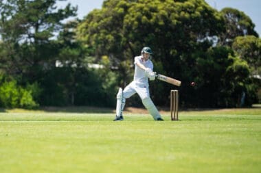 A cricketer is batting on a green cricket oval during a local match in the summer heat of Australia
