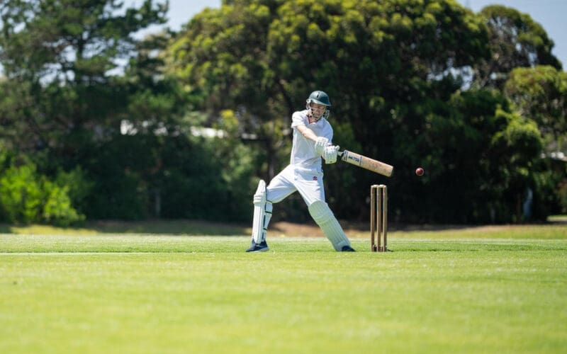 A cricketer is batting on a green cricket oval during a local match in the summer heat of Australia