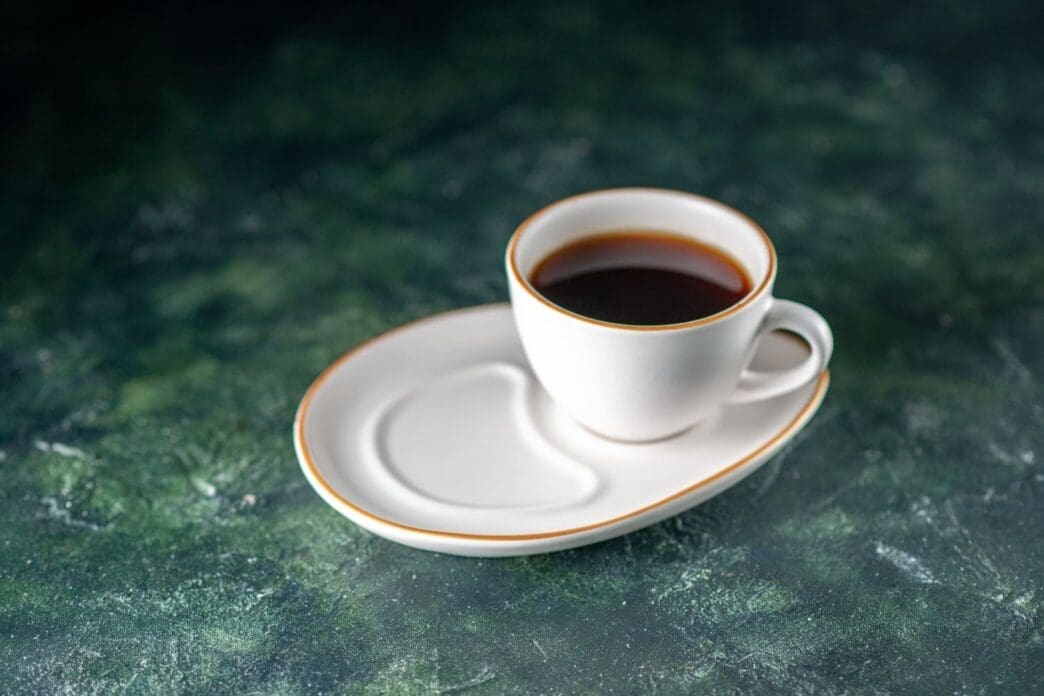A front view of a cup of tea on a white plate resting on a dark surface, perfect for a ceremonial breakfast in the morning