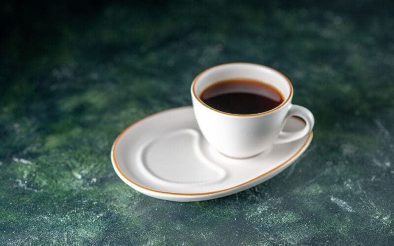 A front view of a cup of tea on a white plate resting on a dark surface, perfect for a ceremonial breakfast in the morning