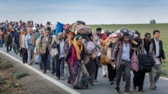 A large group of people are walking down the road with luggage