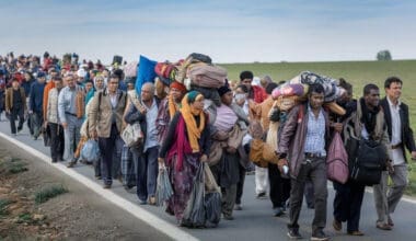 A large group of people are walking down the road with luggage