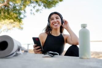 A woman with black hair listens to music on her mobile after finishing her yoga session