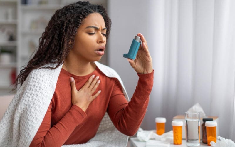 A young Black woman using her inhaler to find relief during an asthma attack