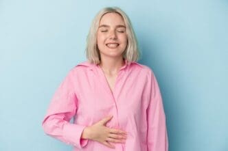A young Caucasian woman gently touches her tummy while smiling softly, despite experiencing a slight discomfort in her upper abdomen