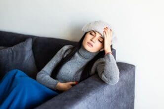 A young woman with migraines is resting on her sofa, a cool, damp towel draped over her forehead.