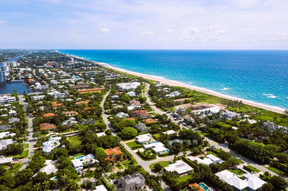 Aerial drone footage highlighting a beachside residential area in South Florida, featuring stunning turquoise waters set against a bright blue sky