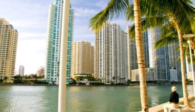 An elderly man relaxes on a bench by Biscayne Bay, taking in the view of the Brickell skyline