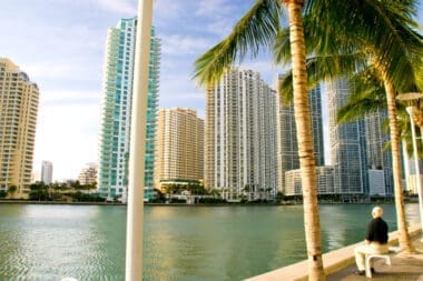 An elderly man relaxes on a bench by Biscayne Bay, taking in the view of the Brickell skyline