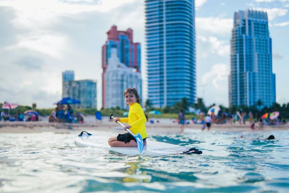 Child enjoying a paddleboard ride during summer vacation at South Pointe Beach