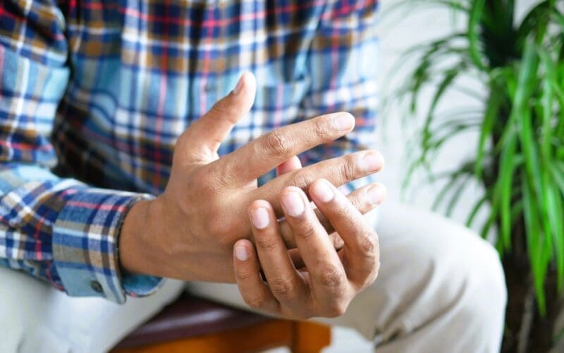 Man experiencing finger pain while seated, due to rheumatoid arthritis