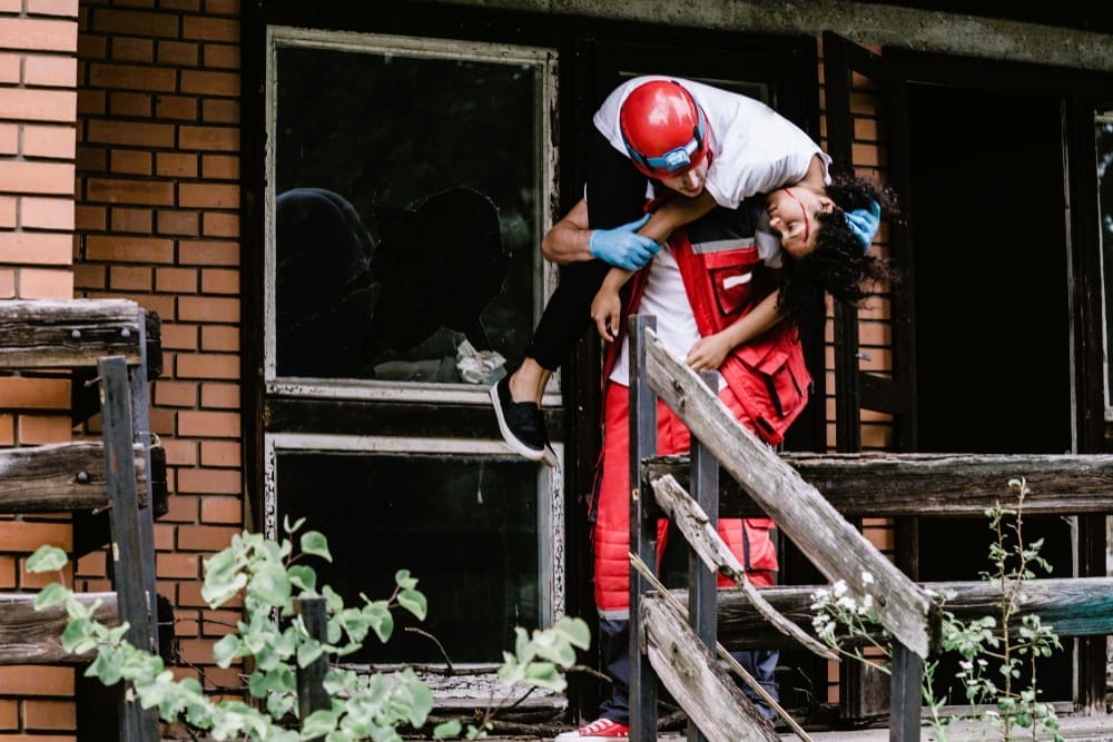 Rescue worker carrying an injured individual from a damaged home