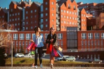 Two girls stroll along city streets, carrying shopping bags on a sunny day