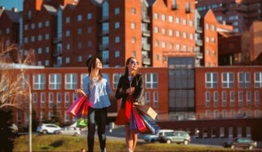 Two girls stroll along city streets, carrying shopping bags on a sunny day