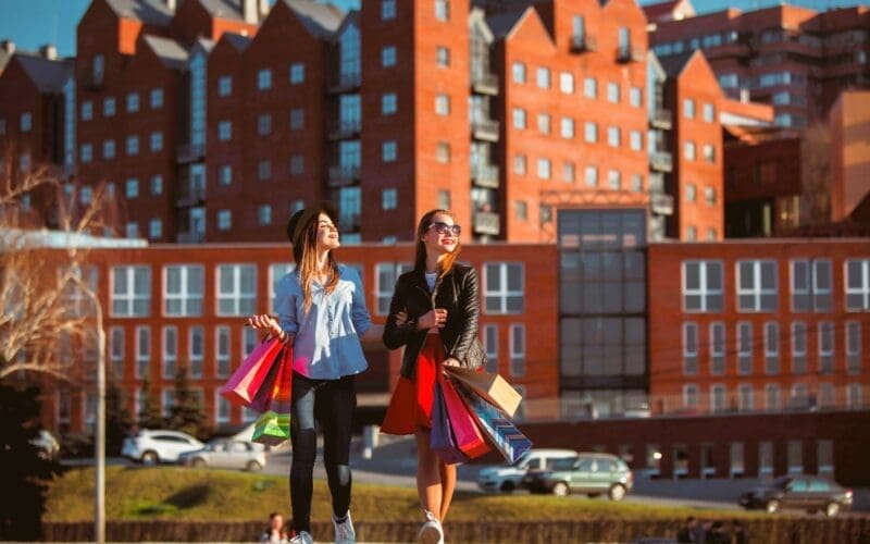 Two girls stroll along city streets, carrying shopping bags on a sunny day