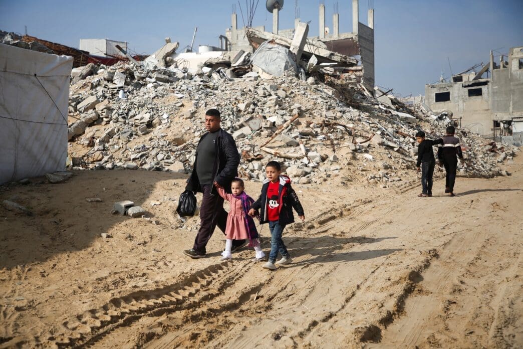 Palestinians walk past the rubble of buildings destroyed in previous Israeli strikes, ahead of a ceasefire set to take effect on Sunday, in Khan Younis