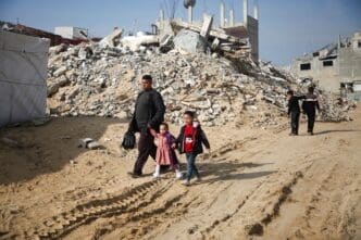 Palestinians walk past the rubble of buildings destroyed in previous Israeli strikes, ahead of a ceasefire set to take effect on Sunday, in Khan Younis