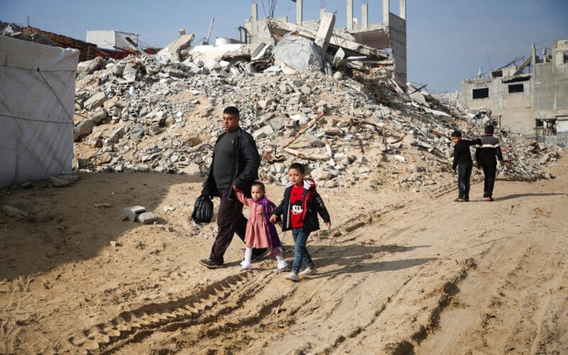 Palestinians walk past the rubble of buildings destroyed in previous Israeli strikes, ahead of a ceasefire set to take effect on Sunday, in Khan Younis
