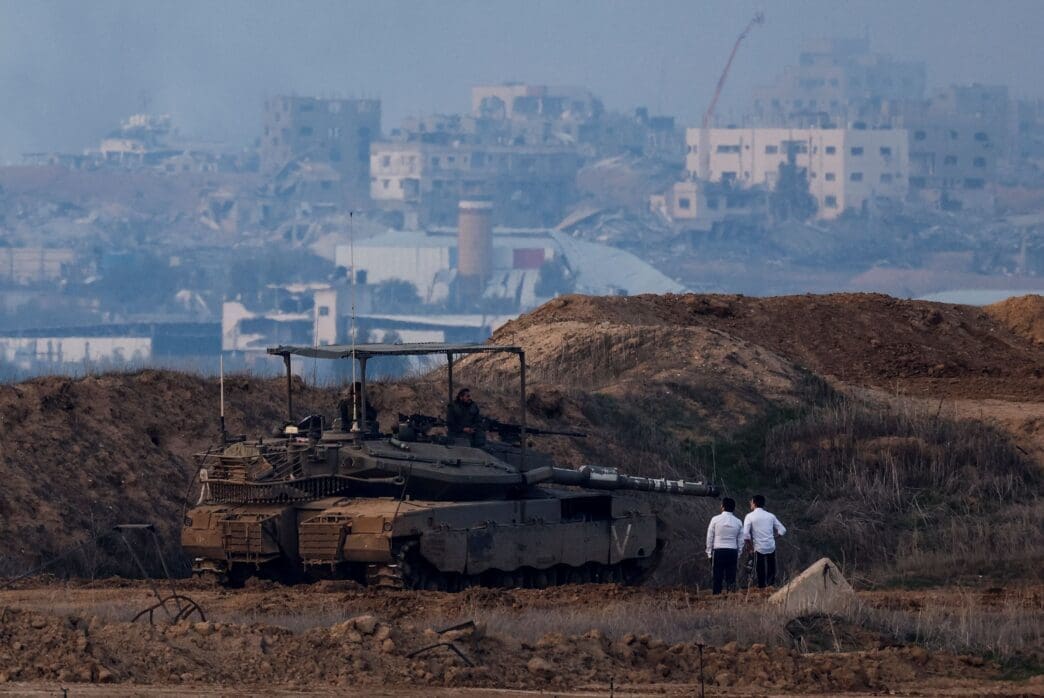 Ultra-Orthodox Jewish men stand near a tank, as seen from the Israeli side of the border