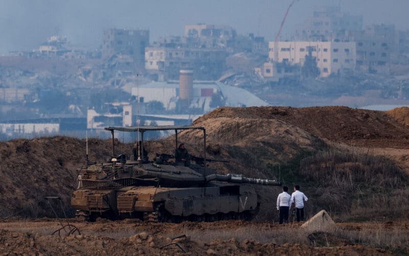 Ultra-Orthodox Jewish men stand near a tank, as seen from the Israeli side of the border
