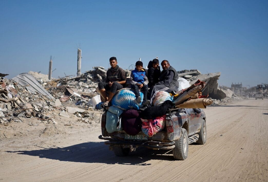 Palestinians ride a vehicle past the rubble of houses and buildings destroyed during the war, in Rafah