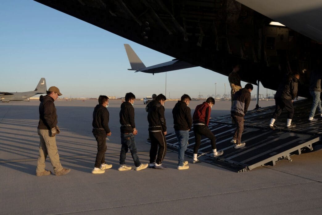 U.S. Customs and Border Protection security agents guide a group of detained migrants to board a removal flight