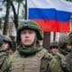 Troops stand in front of the Russian flag