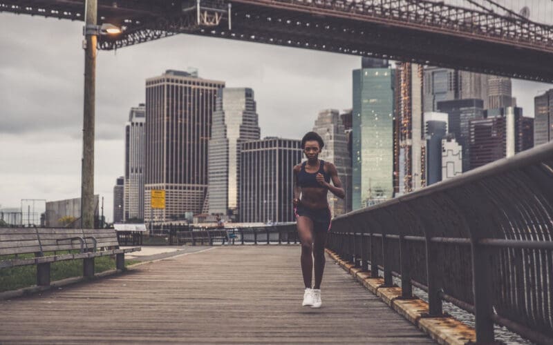 A full-length shot of a woman sprinting swiftly against a backdrop of a city skyline