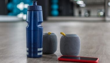 A blue water bottle, portable speakers, and a smartphone resting on the floor of a fitness studio.