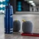 A blue water bottle, portable speakers, and a smartphone resting on the floor of a fitness studio.