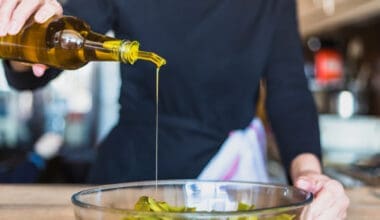 A close-up shot captures a woman's hands skillfully preparing a fresh salad in the kitchen, drizzling seed oil for flavor and nutrition