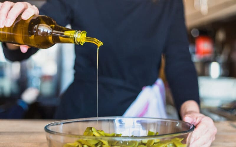 A close-up shot captures a woman's hands skillfully preparing a fresh salad in the kitchen, drizzling seed oil for flavor and nutrition