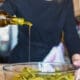 A close-up shot captures a woman's hands skillfully preparing a fresh salad in the kitchen, drizzling seed oil for flavor and nutrition