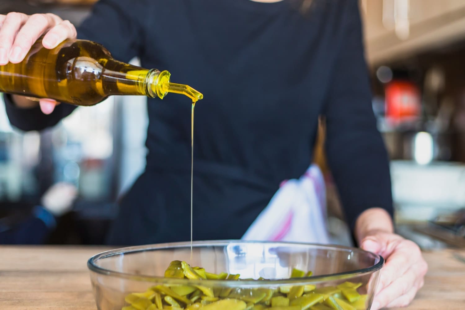 A close-up shot captures a woman's hands skillfully preparing a fresh salad in the kitchen, drizzling seed oil for flavor and nutrition