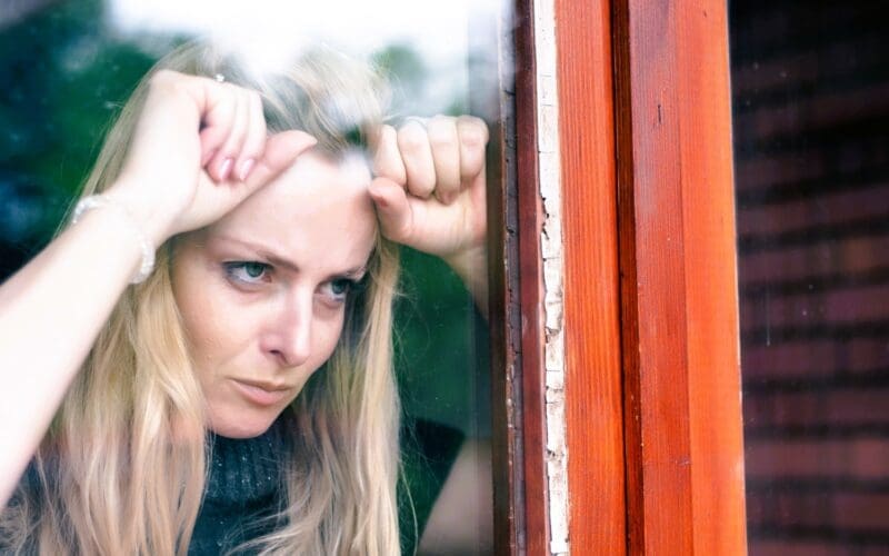 A frustrated woman stands by her window, irritated by the noise from her neighbor