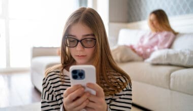 A girl chatting on her cell phone is seen from the front, with her mother seated in the background